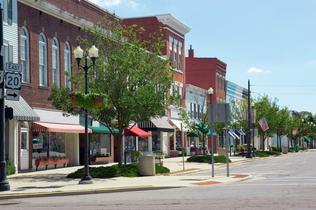 A sunny day on a quiet, tree-lined main street in a small american town, showcasing local shops and classic architecture under a clear blue sky.