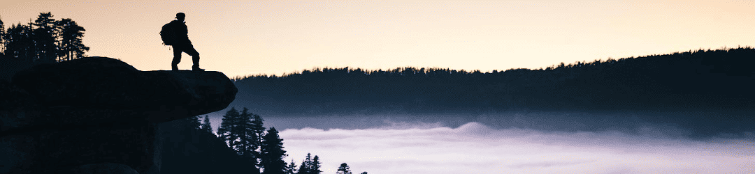 A solitary figure stands on the edge of a cliff, gazing out at a tranquil sea of clouds against the backdrop of a twilight sky.