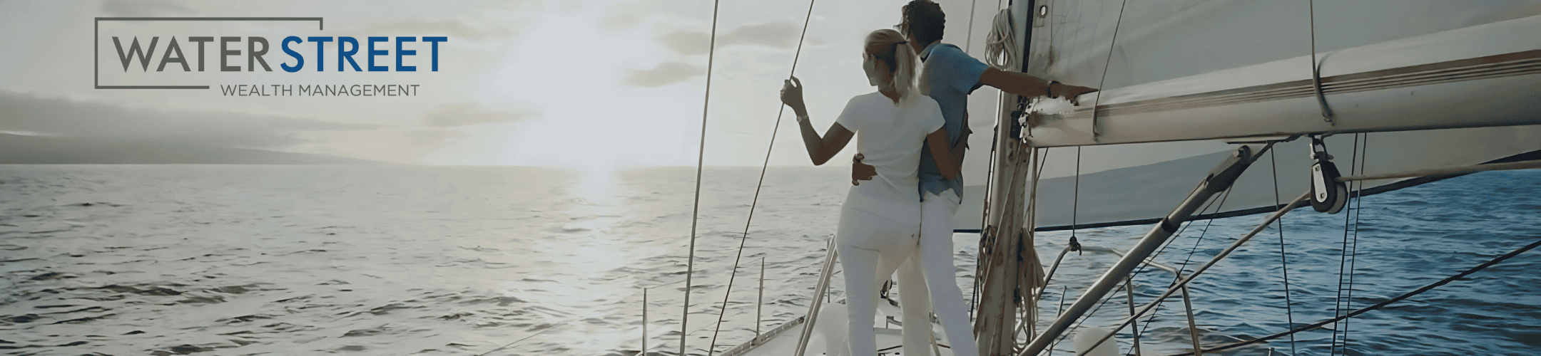 A couple stands together at the edge of a sailboat, looking out at the ocean during sunset. The logo 