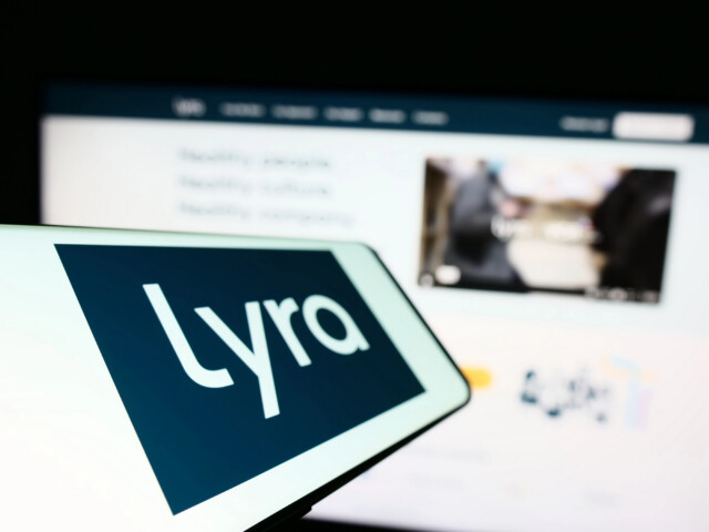 A tablet screen displays the word "Lyra" in large white letters on a dark background, with a blurred computer screen in the background showing text and images.